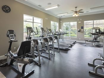 A spacious gym with treadmills, elliptical machines, and a ceiling fan.